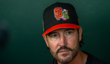A man with a beard wears a black and red baseball cap with an "SF" logo and a colorful snake design, dressed in a matching red and black shirt.