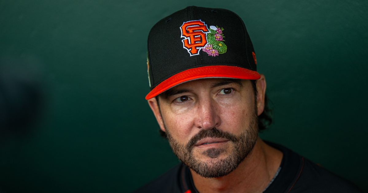 A man with a beard wears a black and red baseball cap with an "SF" logo and a colorful snake design, dressed in a matching red and black shirt.