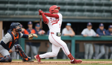 Baseball player swings at home plate.