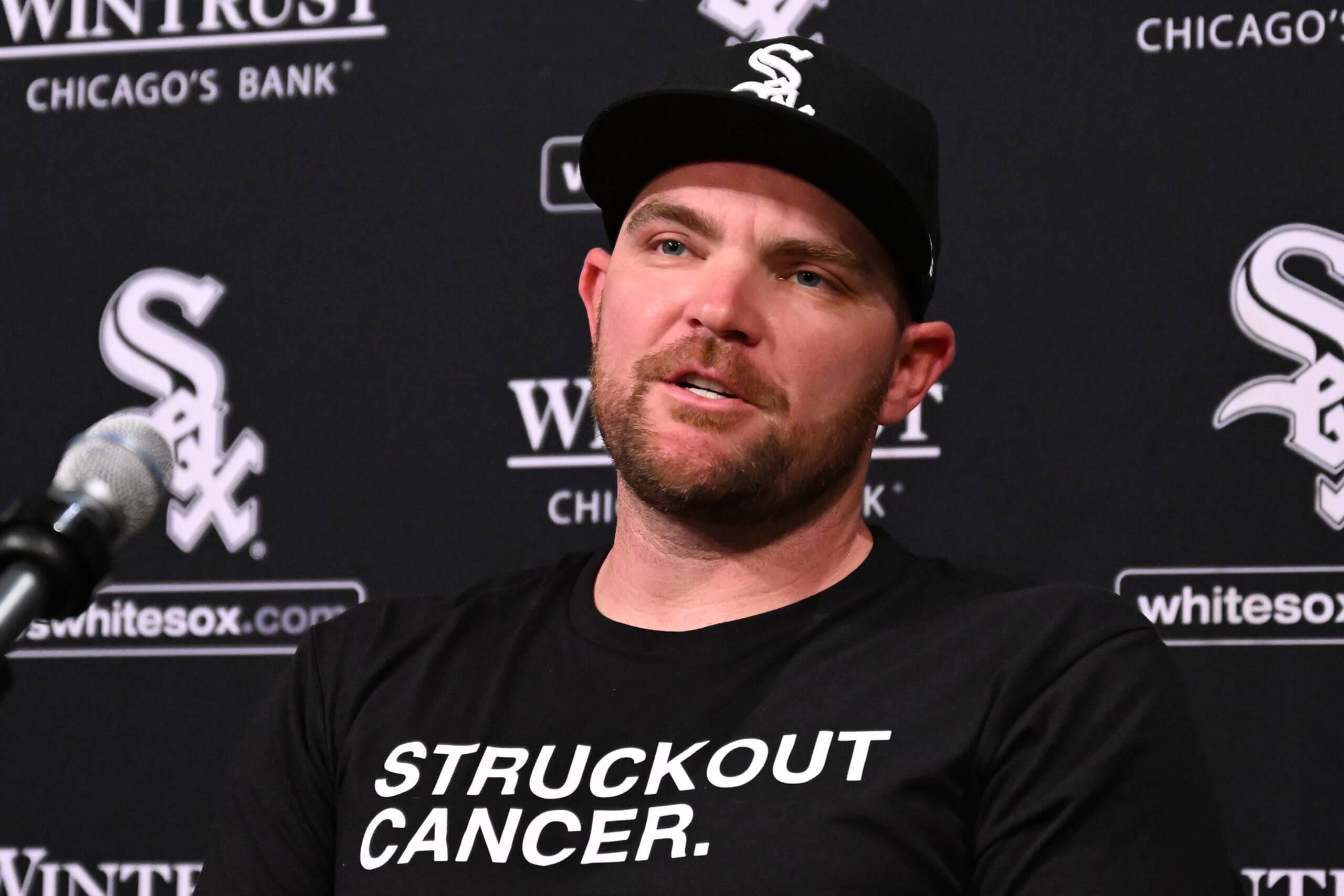 Liam Hendriks, with a black ballcap with white letters and a black T-shirt with white lettering, speaks to reporters.