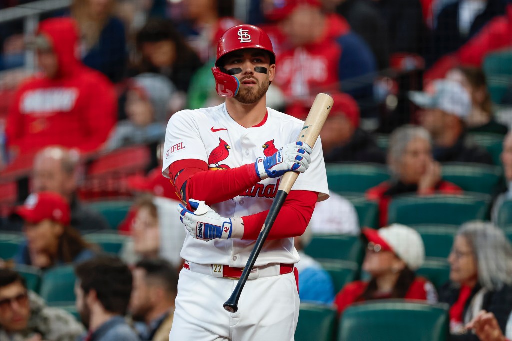 A St. Louis Cardinals player in a red helmet with the team logo, batting gloves, and holding a baseball bat.