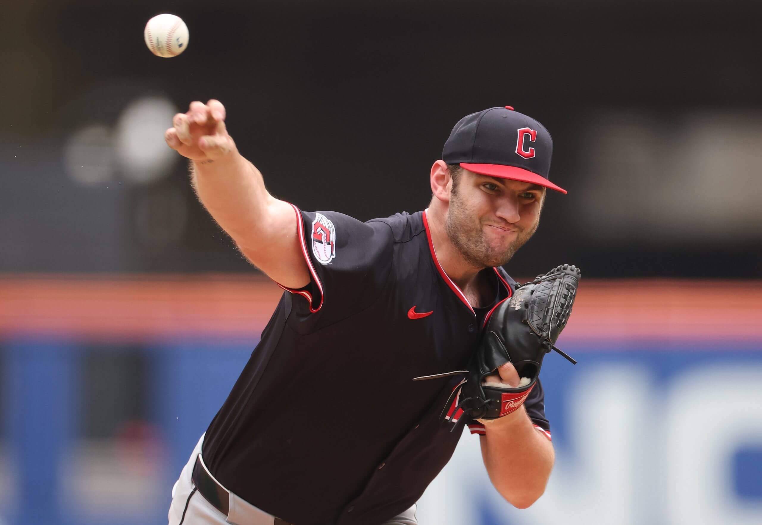 Gavin Williams, in a black jersey and black Guardians hat with a red bill, releases a pitch in a game.