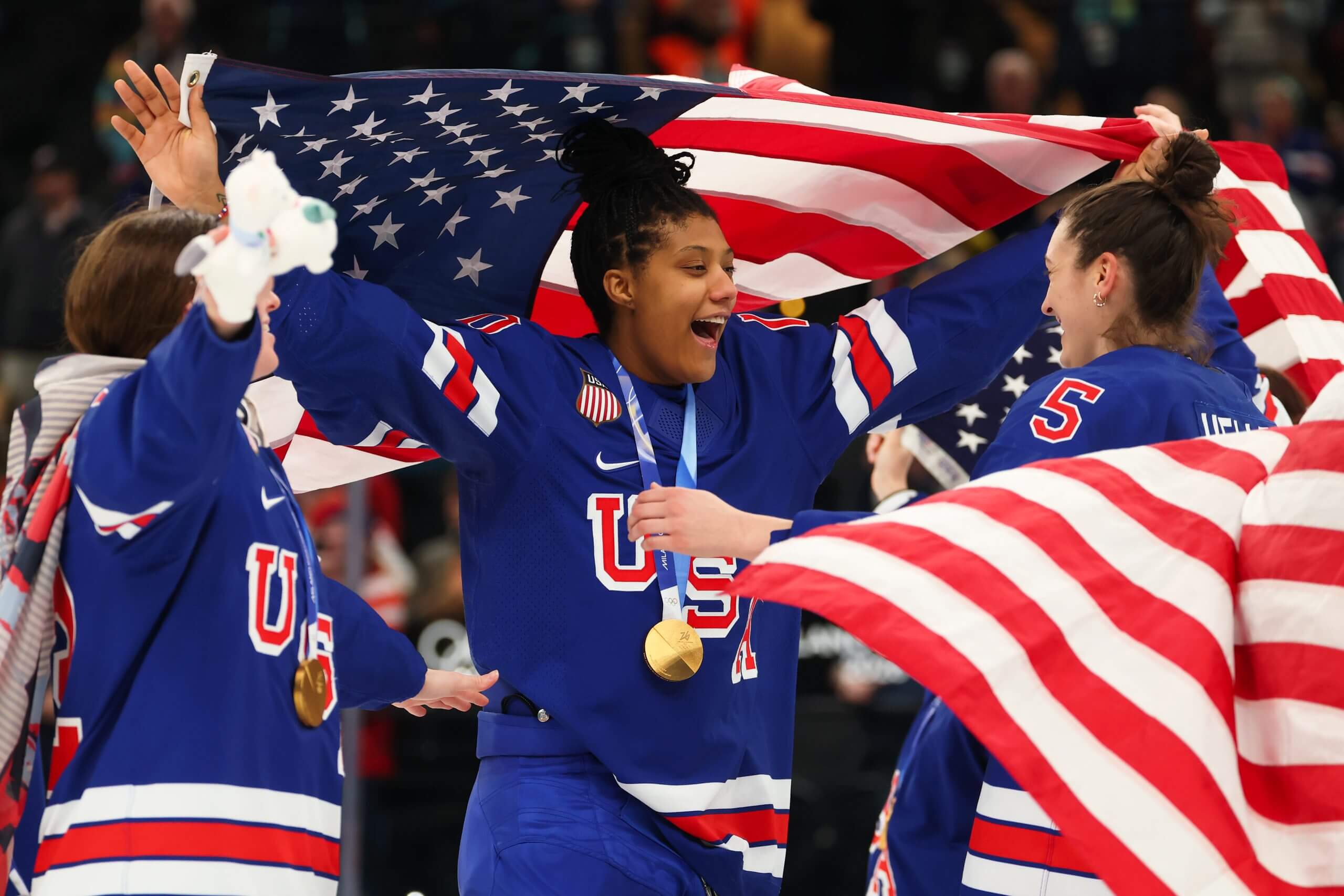 Team USA's Laila Edwards and Megan Keller wave flags and cheer while wearing their gold medals after defeating Canada in women's hockey.