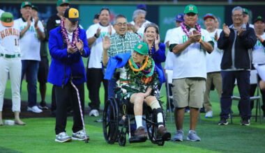 Legendary Hawaii baseball coach Les Murakami waved at the crowd of his namesake stadium as he was presented with a blue College Baseball Hall of Fame jacket and received applause from his old friend and rival Gene Stephenson of Wichita State, front left, and UH legendary pitcher Derek Tatsuno, front right, plus about 50 alumni standing behind him.