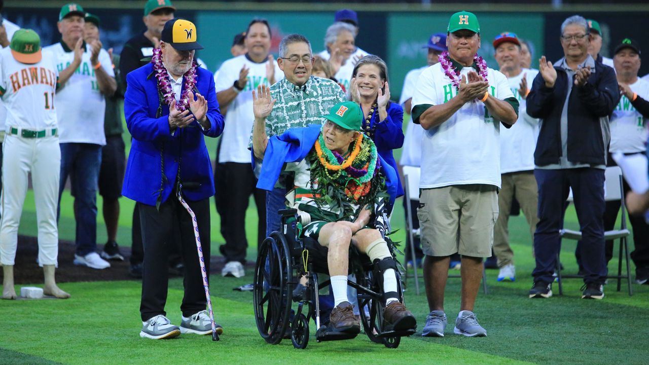 Legendary Hawaii baseball coach Les Murakami waved at the crowd of his namesake stadium as he was presented with a blue College Baseball Hall of Fame jacket and received applause from his old friend and rival Gene Stephenson of Wichita State, front left, and UH legendary pitcher Derek Tatsuno, front right, plus about 50 alumni standing behind him.
