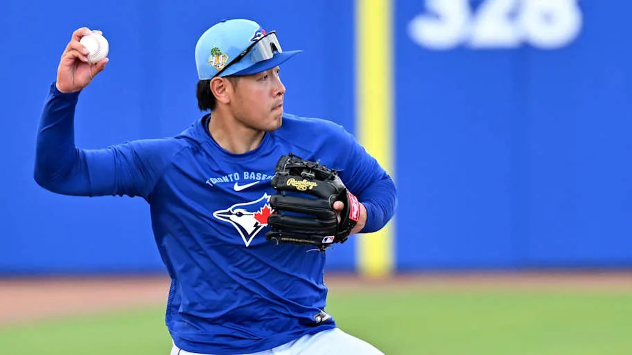 Okamoto throws a baseball in a blue long sleeve Blue Jay