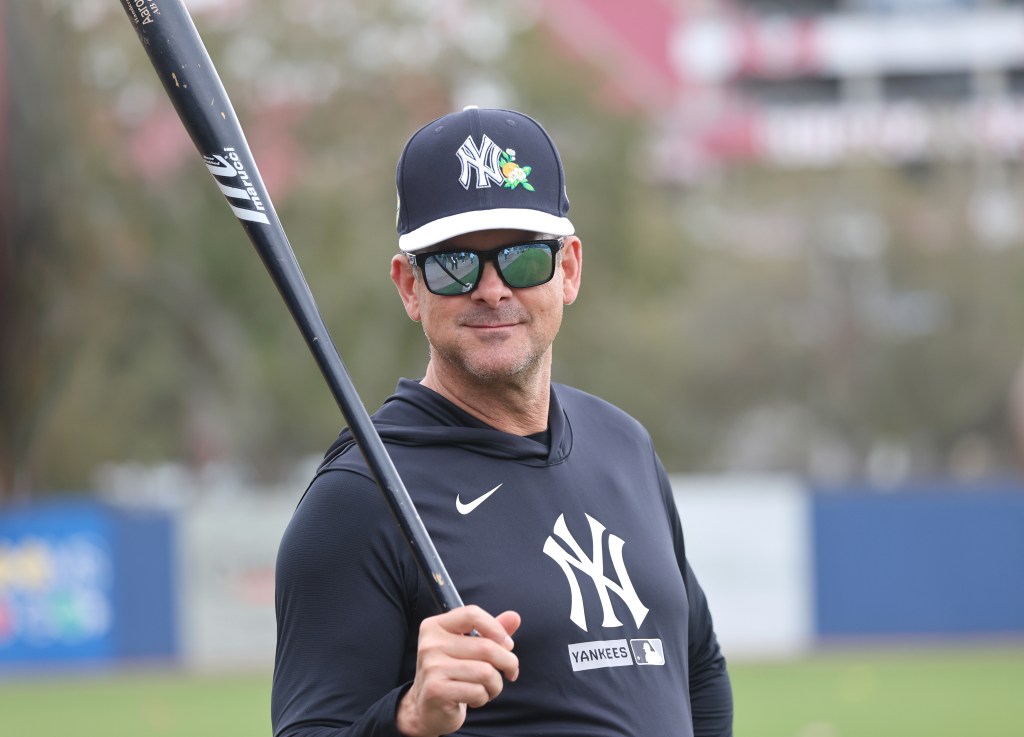 New York Yankees manager Aaron Boone in sunglasses, holding a baseball bat.
