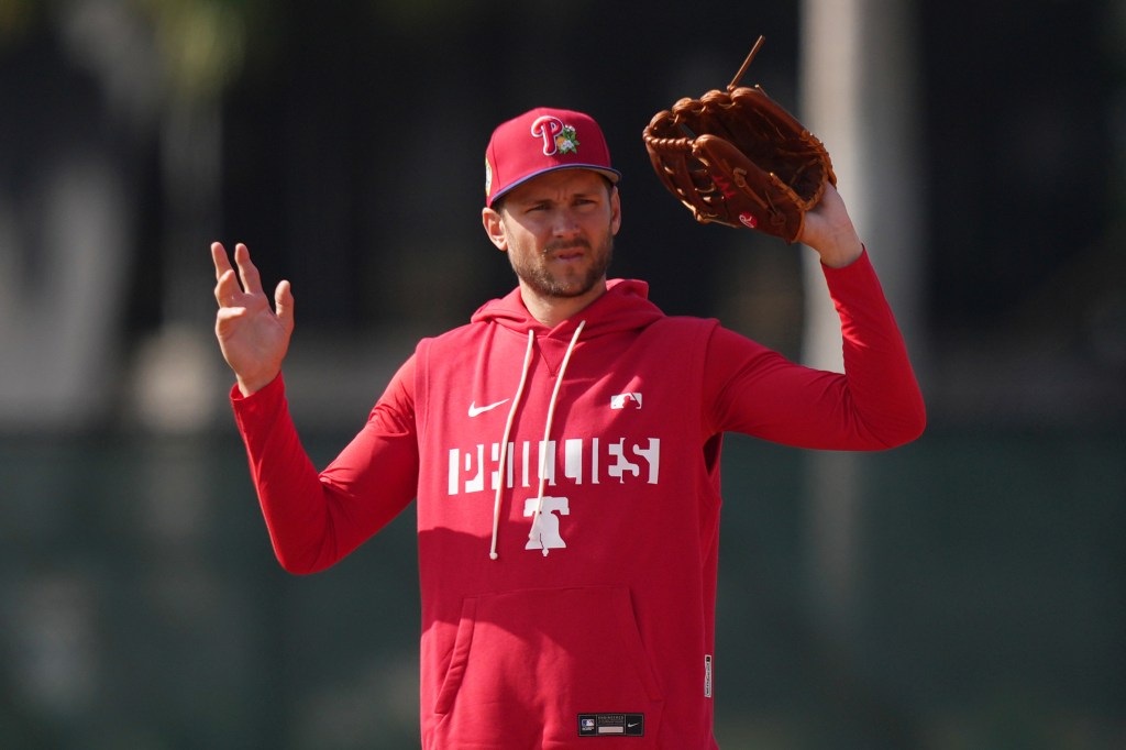 Trea Turner of the Philadelphia Phillies in a red Phillies hoodie and hat holding a baseball glove.