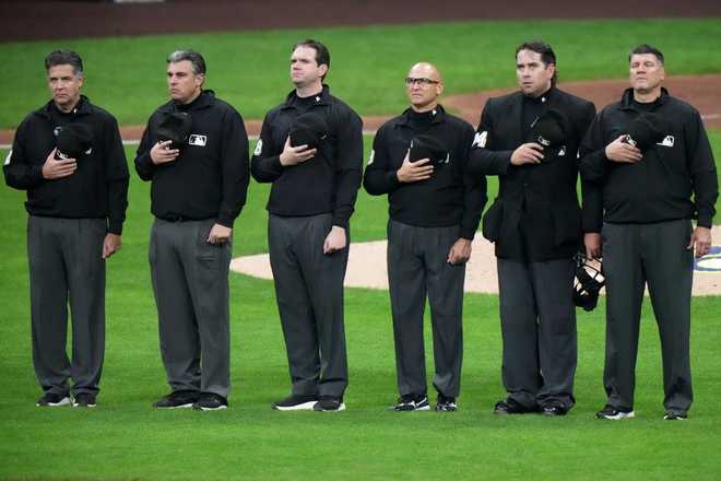 MLB umpires The umpire crew lines up for the singing of "God Bless America," during the seventh inning of Game 1 of baseball's National League Championship Series between the Milwaukee Brewers and the Los Angeles Dodgers Monday, Oct. 13, 2025, in Milwaukee.
