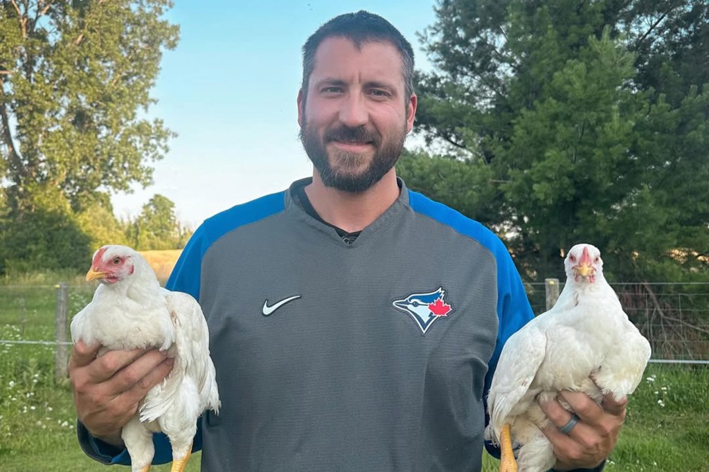 Phillipe Aumont, wearing a Toronto Blue Jays shirt, holds two white chickens.