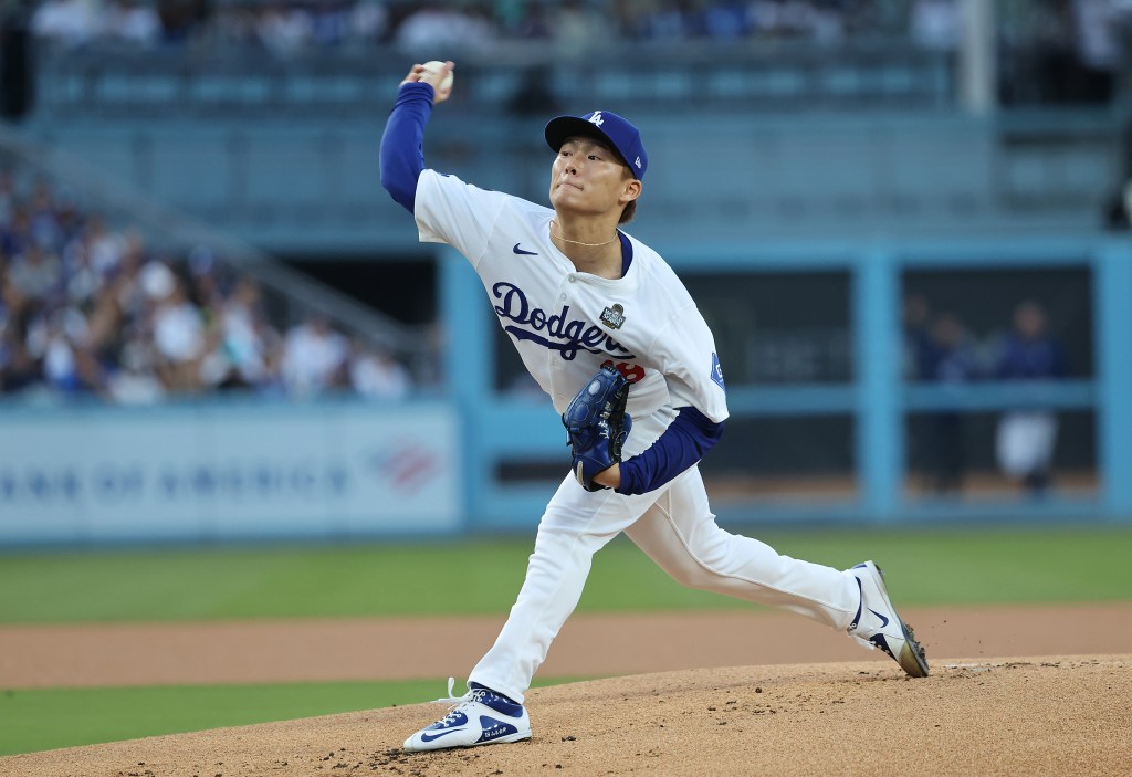 A baseball pitcher in a white uniform with "Dodgers" written across the chest throws a pitch from a mound.
