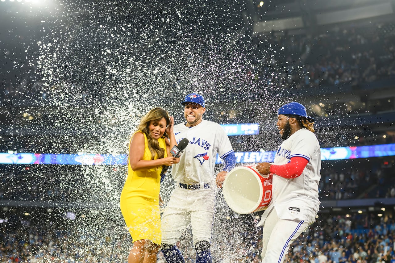 A woman in a yellow dress has a cooler of Gatorade dumped on her by two baseball players.