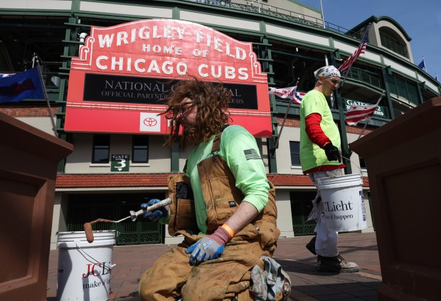 John Jacobs, left, and Jeff Brulle of Painters Local 147 paint flower planters in front of the marquee at Wrigley Field, March 25, 2026, ahead of opening day between the Chicago Cubs and Washington Nationals. (John J. Kim/Chicago Tribune)