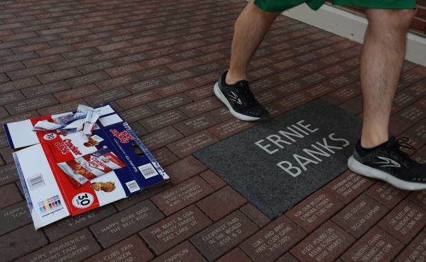 A Cracker Jack box lies on the ground next to a brick displaying Ernie Banks' name on the Waveland Avenue side of Wrigley Field on March 25, 2026. (John J. Kim/Chicago Tribune)
