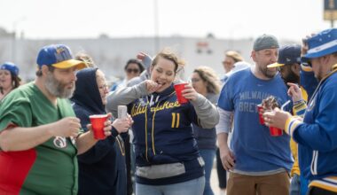 A group of people wearing Milwaukee Brewers apparel gather outdoors, holding red cups and socializing before a game.
