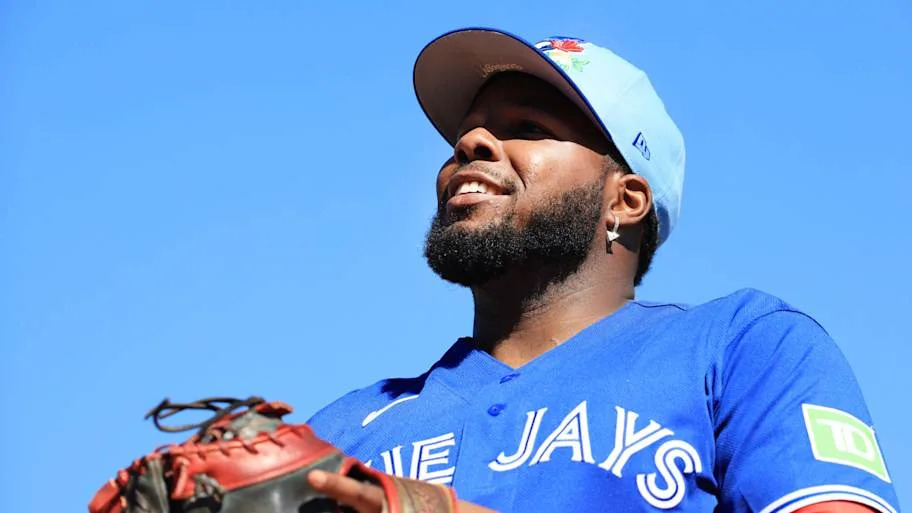 Guerrero Jr. smiles holding a glove in a blue Blue Jays jerse