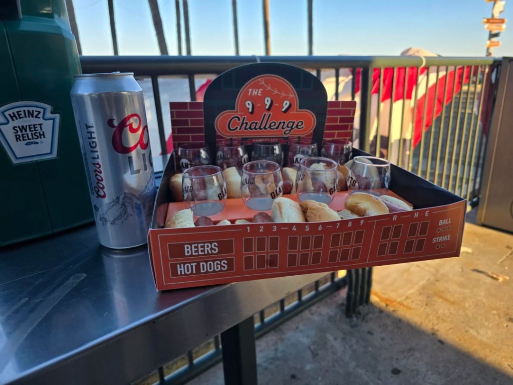 A Coors Light can next to a "9-9-9 Challenge" tray with 9 glasses and 9 hot dog buns with wieners.