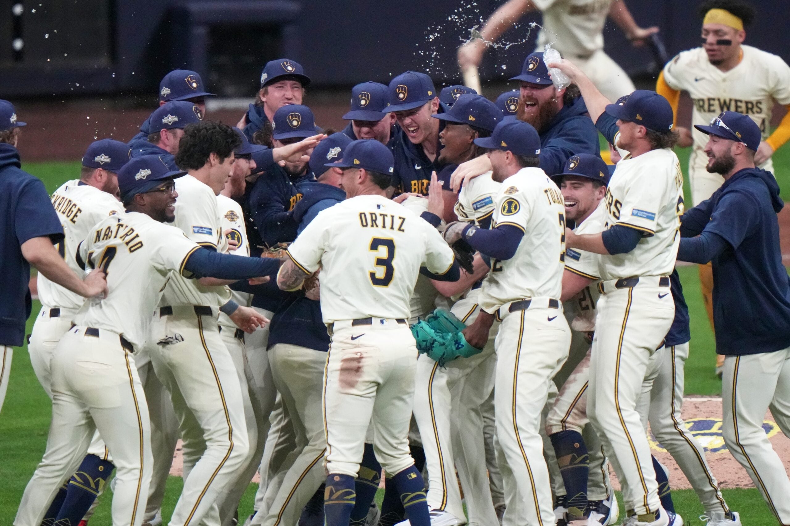 A group of Milwaukee Brewers baseball players in uniforms celebrate together on the field, with some pouring water over a teammate in the center.