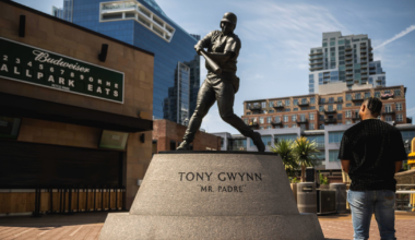 A bronze statue of baseball player Tony Gwynn in batting stance stands on a pedestal labeled "Mr. Padre" with a man looking at it nearby.