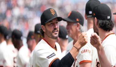 San Francisco Giants players in white jerseys and black caps greet each other with fist bumps during a game in a crowded stadium.