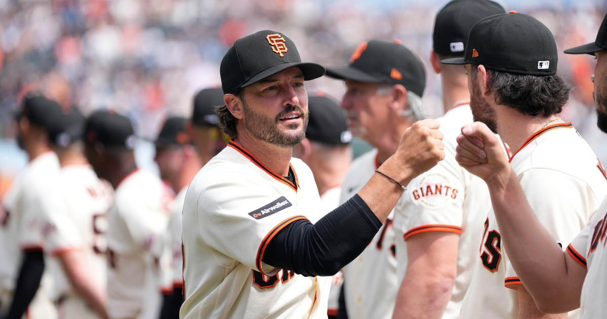 San Francisco Giants players in white jerseys and black caps greet each other with fist bumps during a game in a crowded stadium.