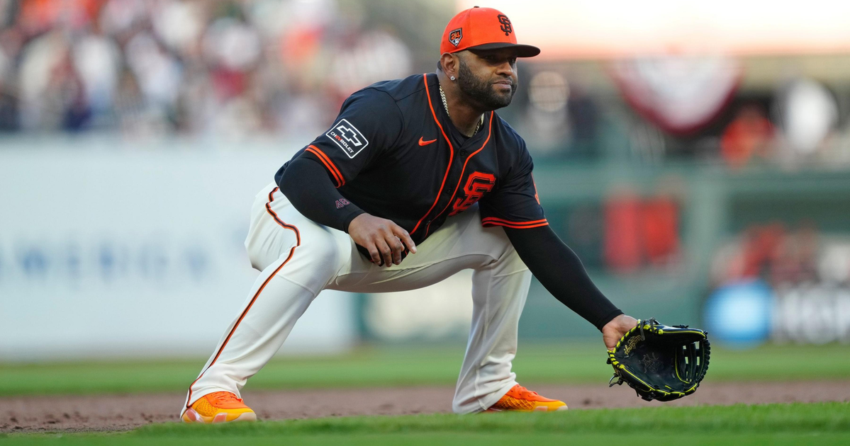 A baseball player in a black and orange San Francisco Giants uniform crouches in a ready fielding position on the infield dirt.