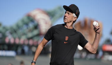 A man in a black San Francisco Giants shirt and cap prepares to throw a baseball on a sunny day at a stadium.