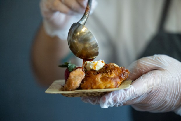 A chef pours ancho syrup over a Chicken & Churros dish during the Taste of Wrigley Field event on March 20, 2026. The dish includes fried chicken, churros, ancho syrup and strawberries. (Josh Boland/Chicago Tribune)