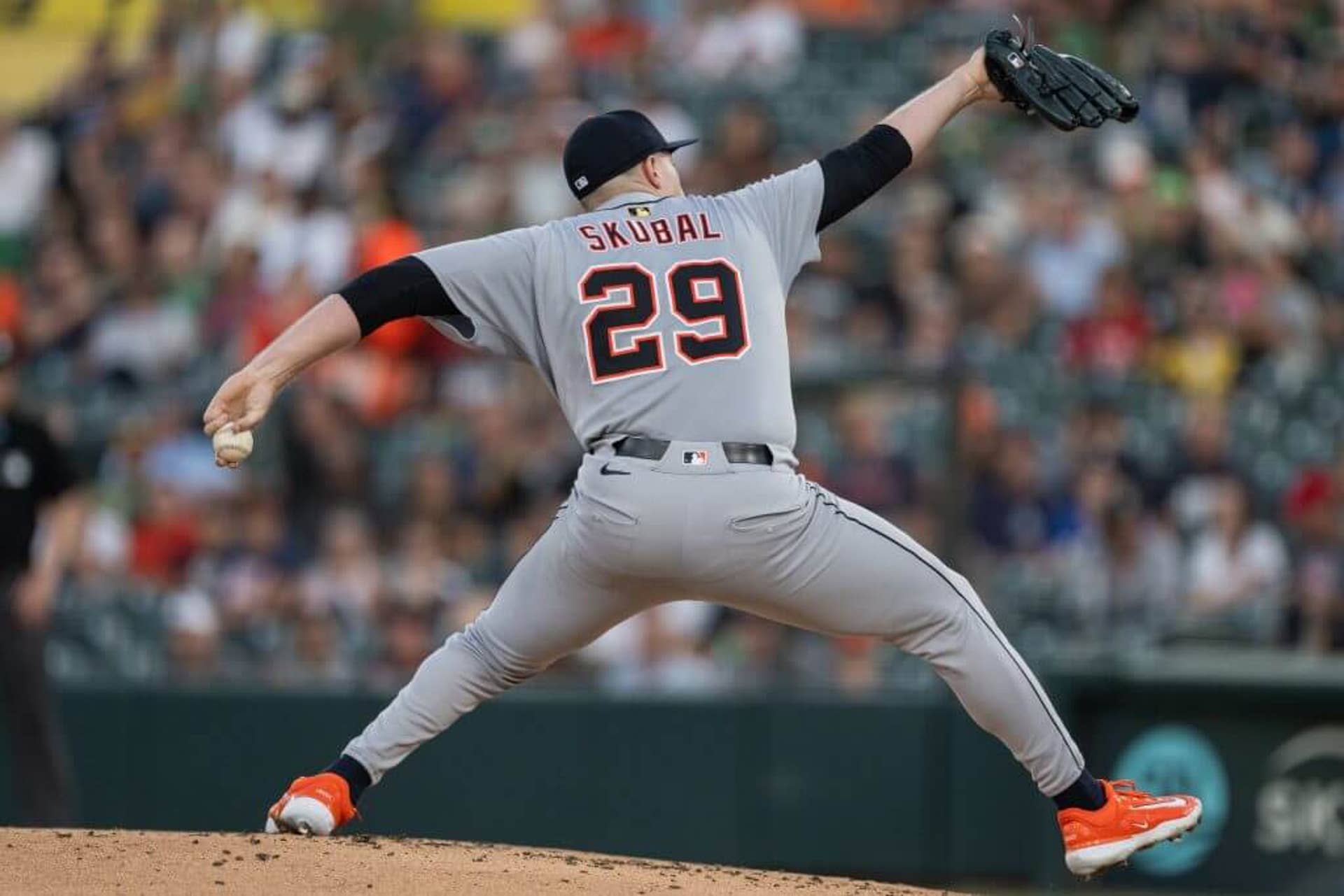 Detroit pitcher Tarik Skubal, donning a gray Tigers uniform with a black hat, reaches full extension as he prepares to deliver a pitch towards home plate.
