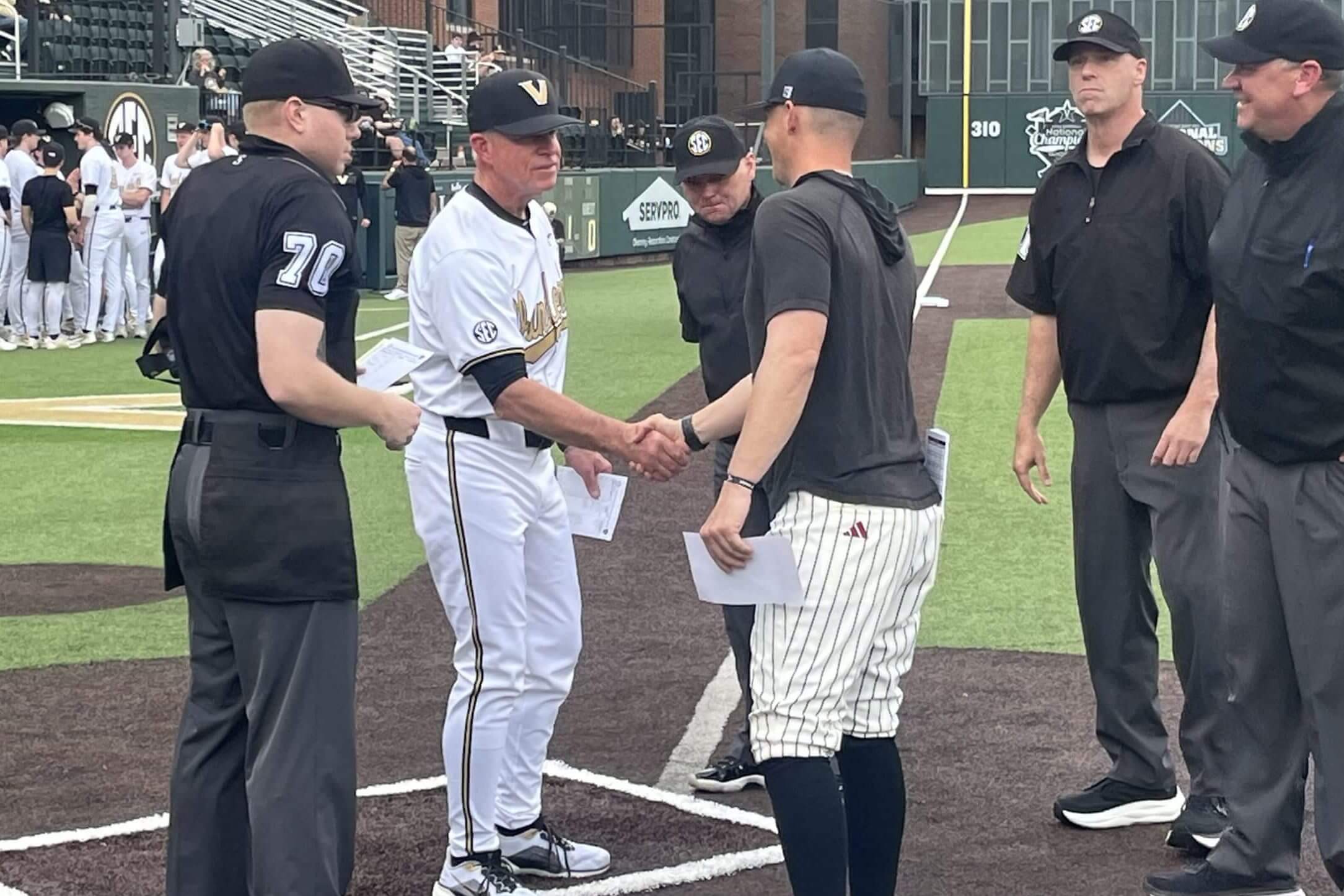 The Vanderbilt and Troy head coaches shake hands at the plate, surrounded by the umpiring crew, before the game.