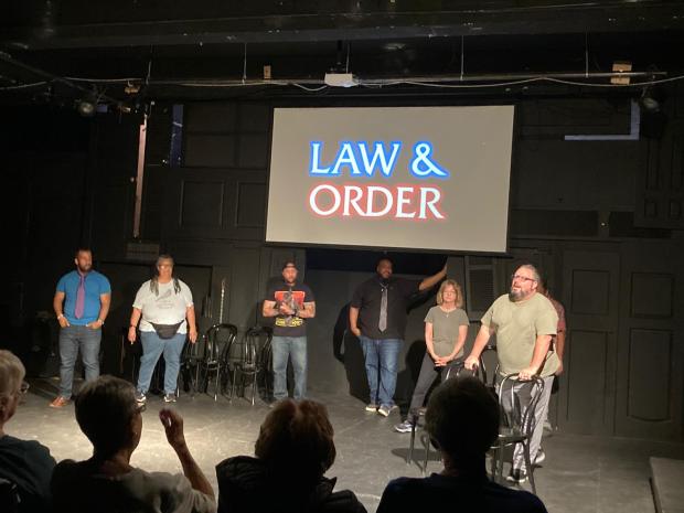 The cast of Law and Order SIU: Special Improv Unit seek an audience member to play the victim. Cast pictured left to right are AJ McCombs, Kasey Jones, Lloyd Scott, Carlton Kearney, Gail Vogler Schuman, Michael Harris and Joshua Reynolds. (Courtesy of MidAtlantic Improv)