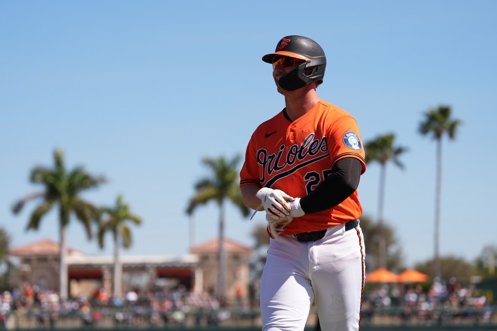 Pete Alonso in an orange Orioles uniform, with a black helmet and sunglasses, walks off the field.