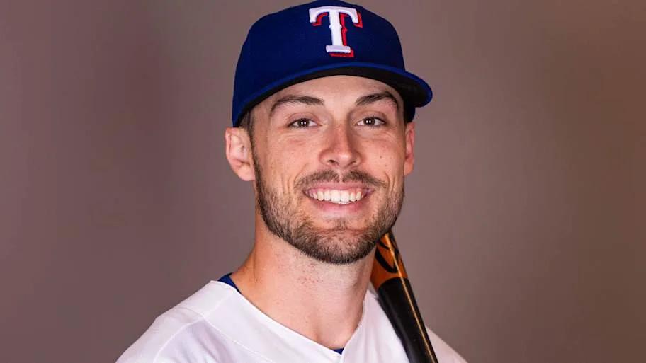 Texas Rangers outfielder Evan Carter poses for a photo with a bat on his shoulder.
