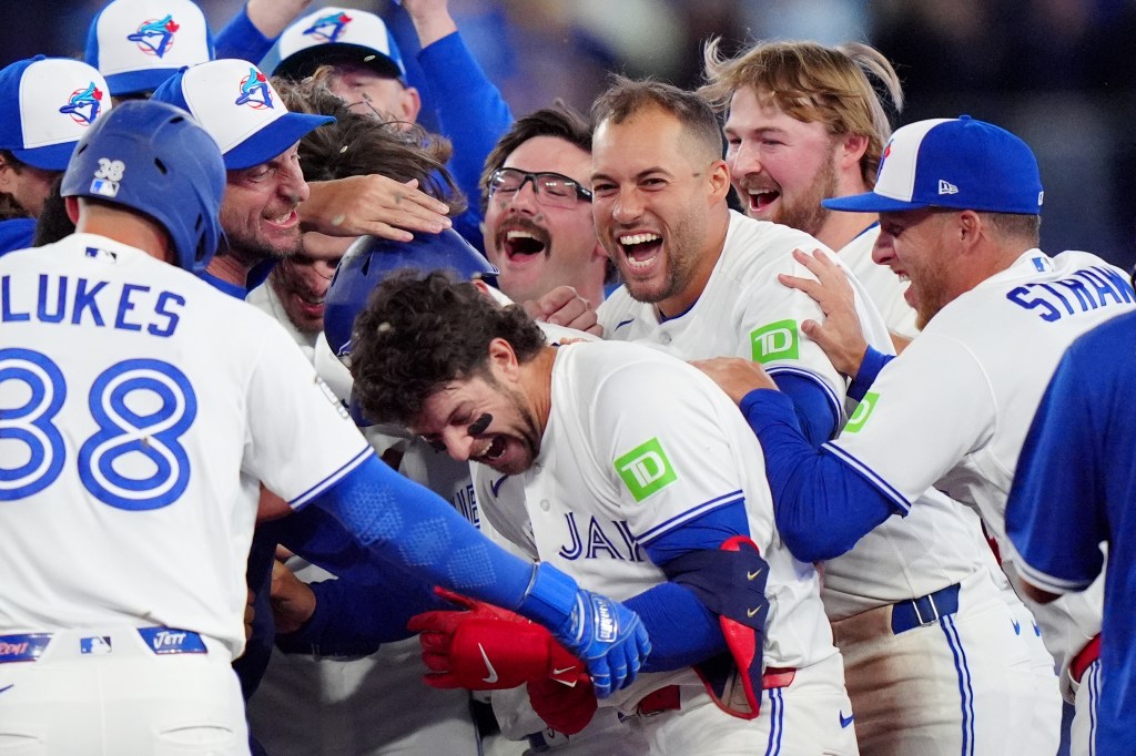 Toronto Blue Jays players celebrate a win, with several cheering around a teammate in the center.