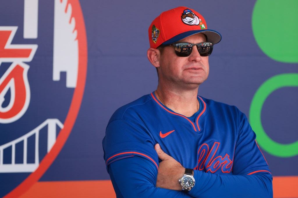 New York Mets manager Carlos Mendoza wearing a red baseball cap and sunglasses.