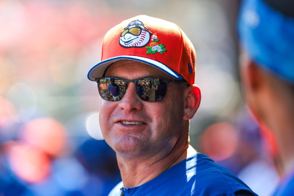New York Mets manager Carlos Mendoza wearing a red baseball cap and sunglasses.