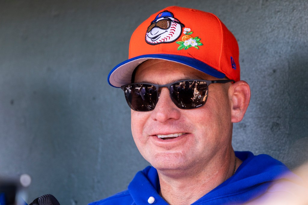 New York Mets manager Carlos Mendoza in an orange cap and sunglasses talks in the dugout.