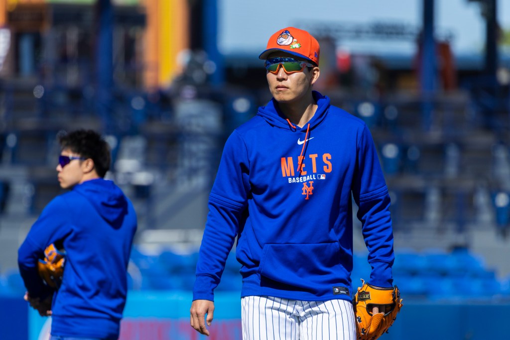 New York Mets pitcher Kodai Senga in a blue sweatshirt and orange cap and sunglasses on the field.
