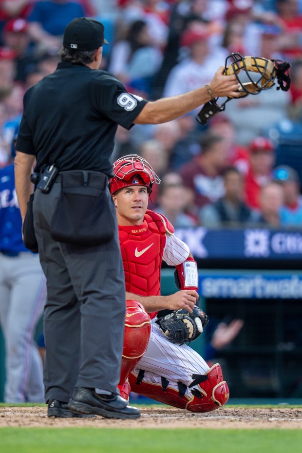 Umpire James Hoye, left, tells Philadelphia Phillies catcher J.T. Realmuto, right, that relief pitcher Zach Pop called for the ABS challenge during the seventh inning of an Opening Day game against the Texas Rangers, Thursday, March 26, 2026, in Philadelphia. (AP Photo/Chris Szagola)