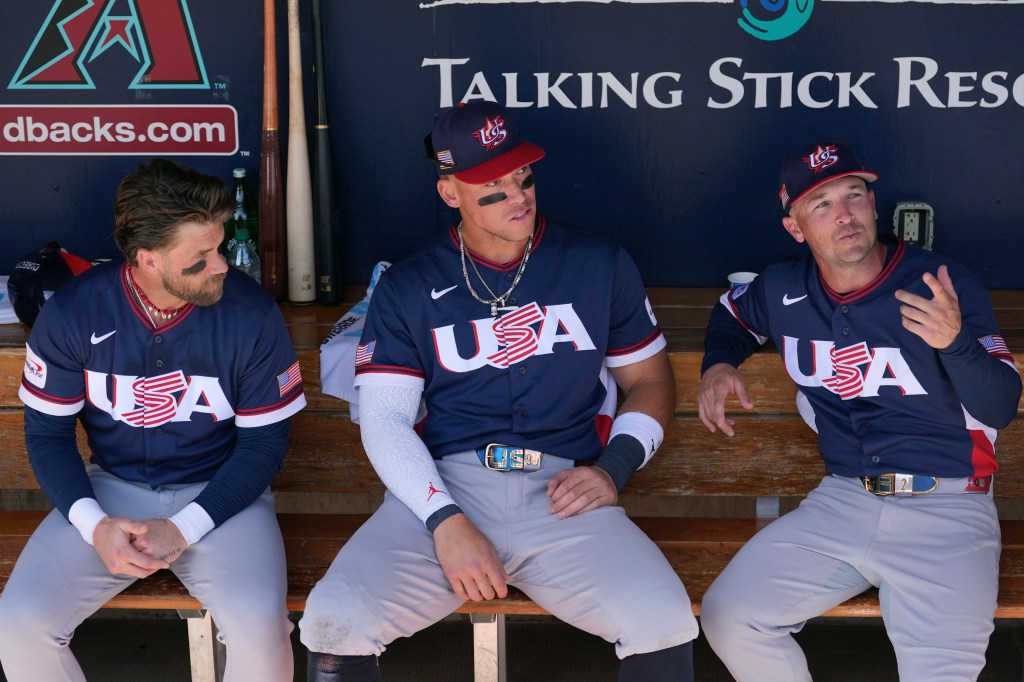 United States' Bryce Harper, left, Aaron Judge, center, and Alex Bregman sit in the team dugout prior to an exhibition baseball game against the Colorado Rockies Wednesday, March 4, 2026, in Scottsdale, Ariz. 