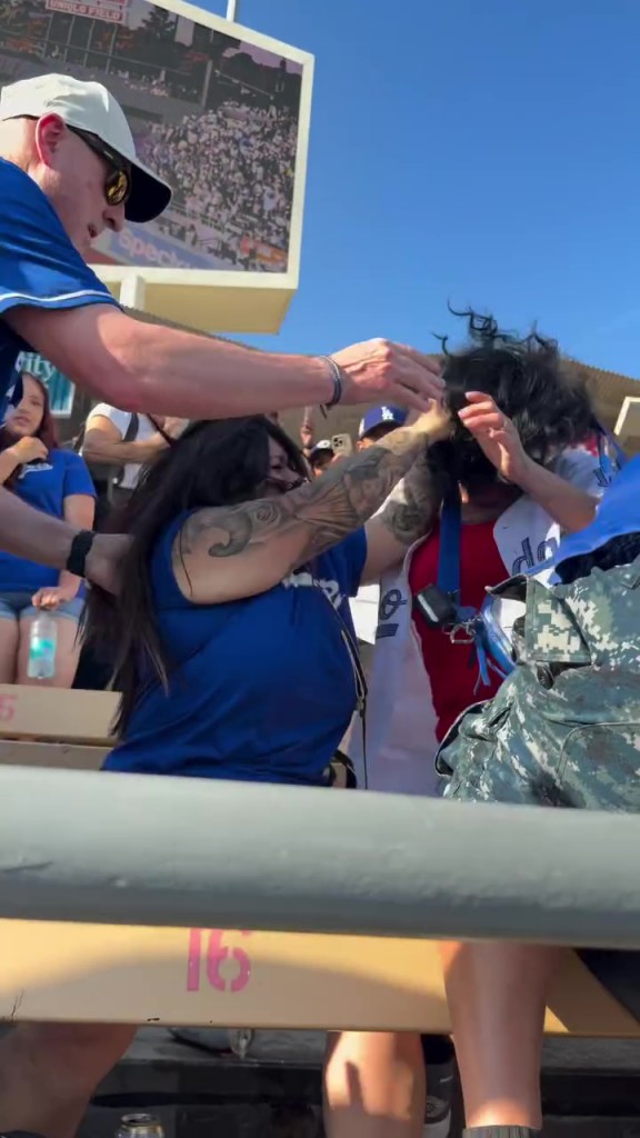 A man with sunglasses and a hat intervenes in a brawl between two women in a stadium.