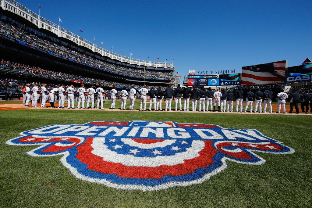 Baseball players on the field at Yankee Stadium with an "OPENING DAY" logo painted on the grass.