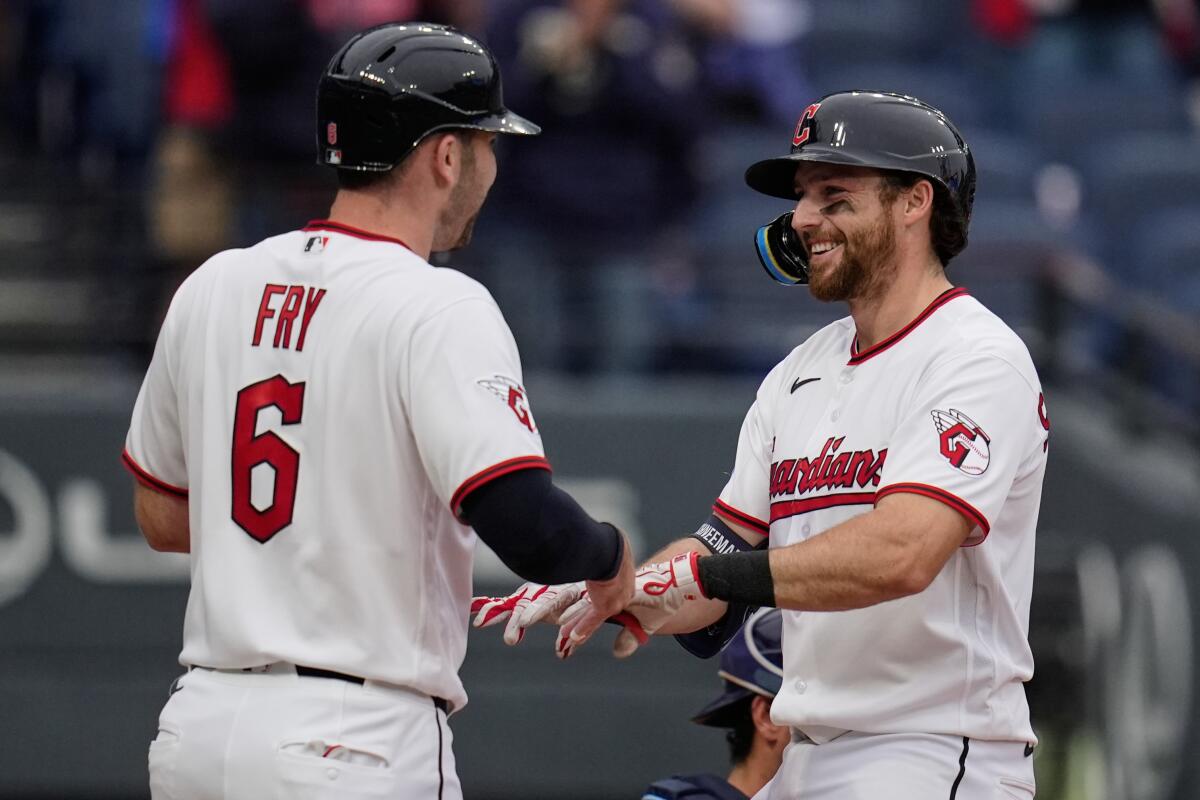 Two baseball players wearing batting helmets smile and bump hands