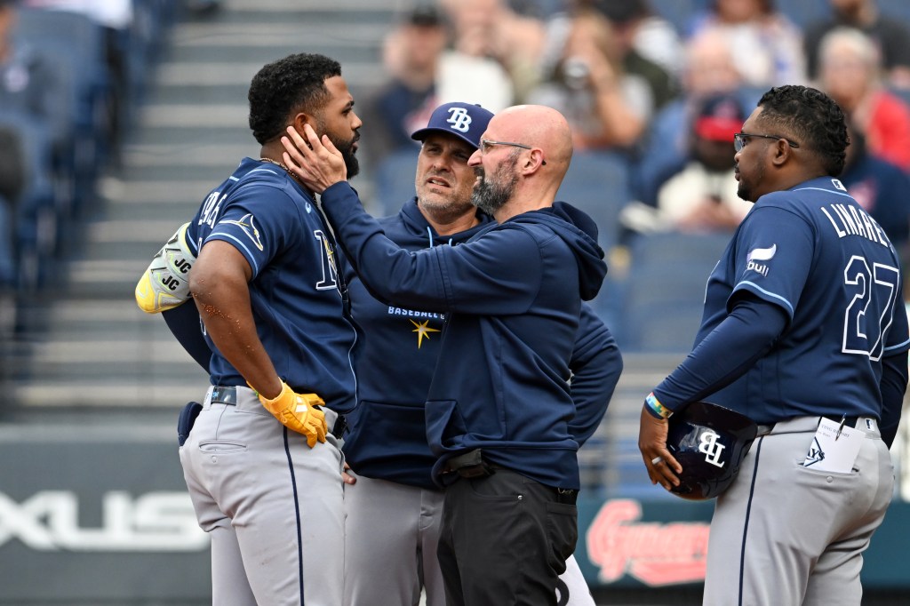 A trainer touches the face of a Tampa Bay Rays player as another player and coach look on during a game against the Cleveland Guardians.