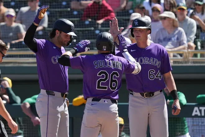 Mar 6, 2026; Mesa, Arizona, USA; Colorado Rockies catcher Brett Sullivan (26) celebrates with third baseman Kyle Karros (12) and first baseman T.J. Rumfield (64) after hitting a three run home run against the Athletics in the first inning at Hohokam Stadium.