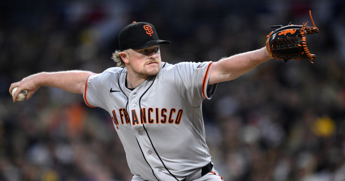 A San Francisco Giants pitcher is mid-throw, wearing a gray uniform and black cap, focused intently on the target during a game.