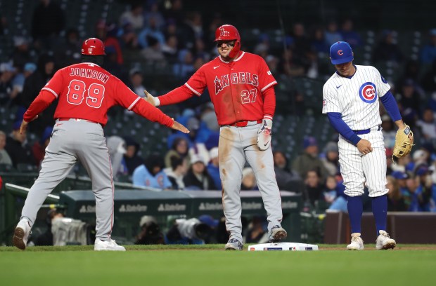 Los Angeles Angels center fielder Mike Trout (27) high-fives third base coach Keith Johnson (89) at third base while standing beside Chicago Cubs third baseman Alex Bregman in the first inning of a game at Wrigley Field in Chicago on March 31, 2026. (Chris Sweda/Chicago Tribune)