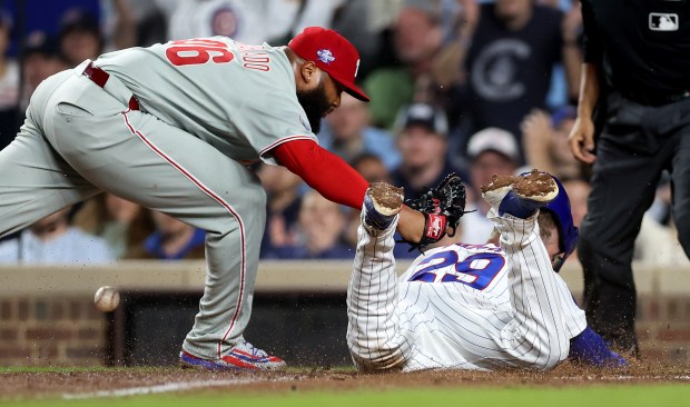 Philadelphia Phillies relief pitcher José Alvarado (46) applies a tag without securing the ball in his glove as Chicago Cubs first baseman Michael Busch slides in to score on a wild pitch in the eighth inning of a game at Wrigley Field in Chicago on April 21, 2026. (Chris Sweda/Chicago Tribune)