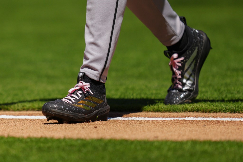 Baseball player Brandon Pfaadt walks on the field, showing his black and gold cleats with pink laces.