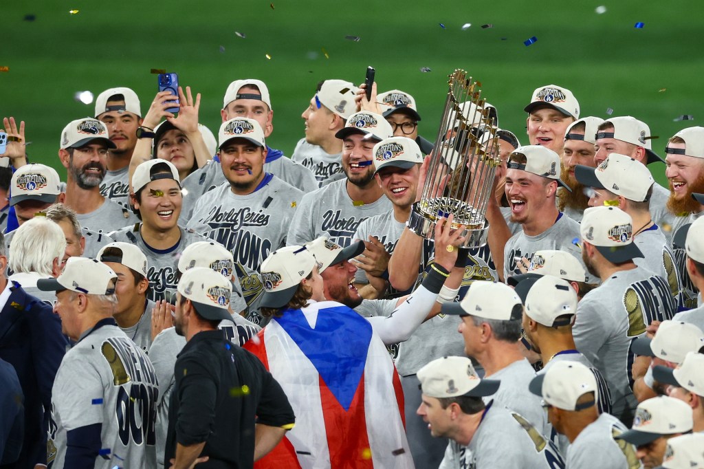 Miguel Rojas of the Los Angeles Dodgers holds the Commissioner's Trophy as his team celebrates winning the 2025 World Series.